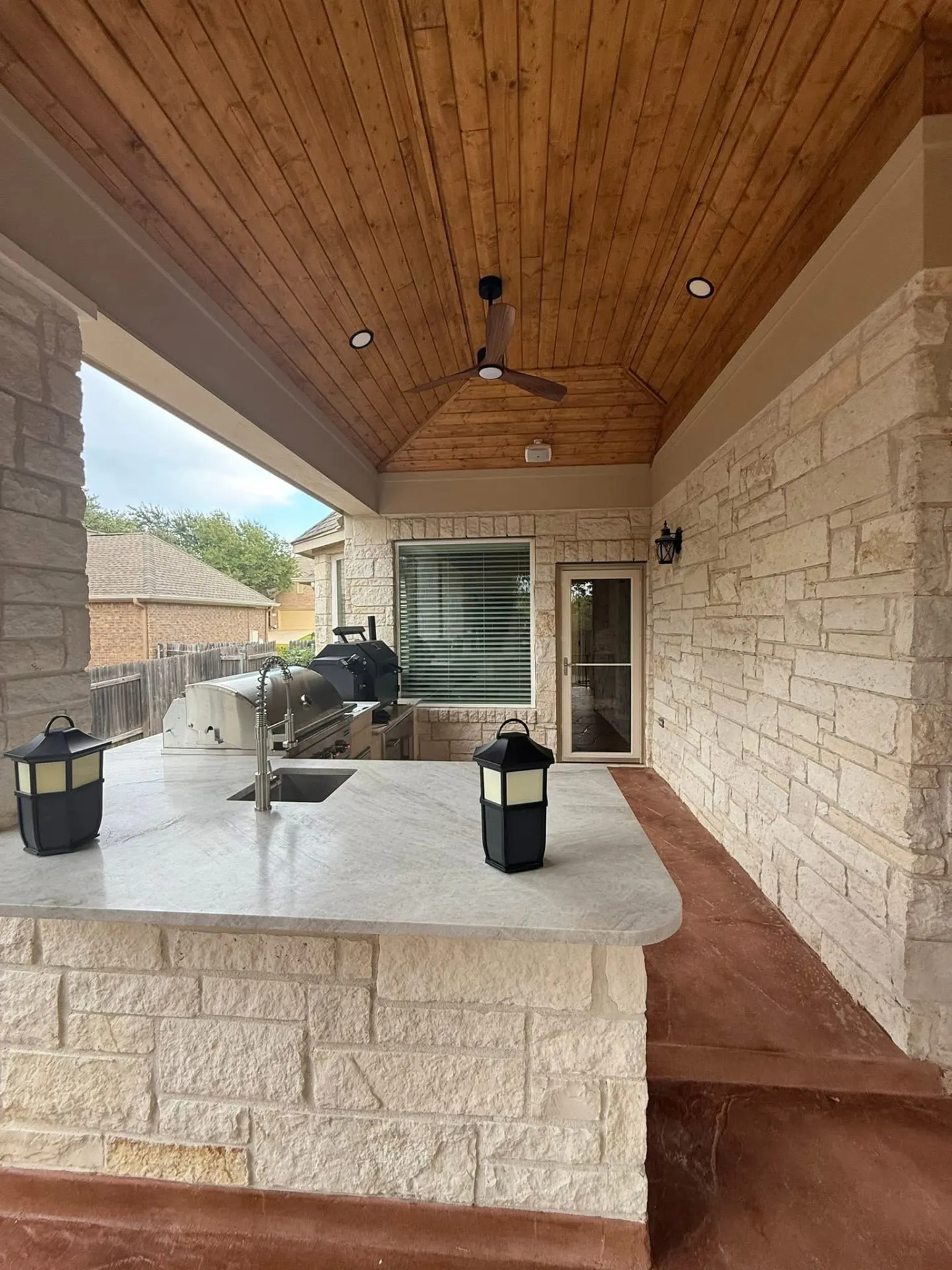Built-in outdoor kitchen with stone bar seating and stained wood ceiling on a covered TWT patio