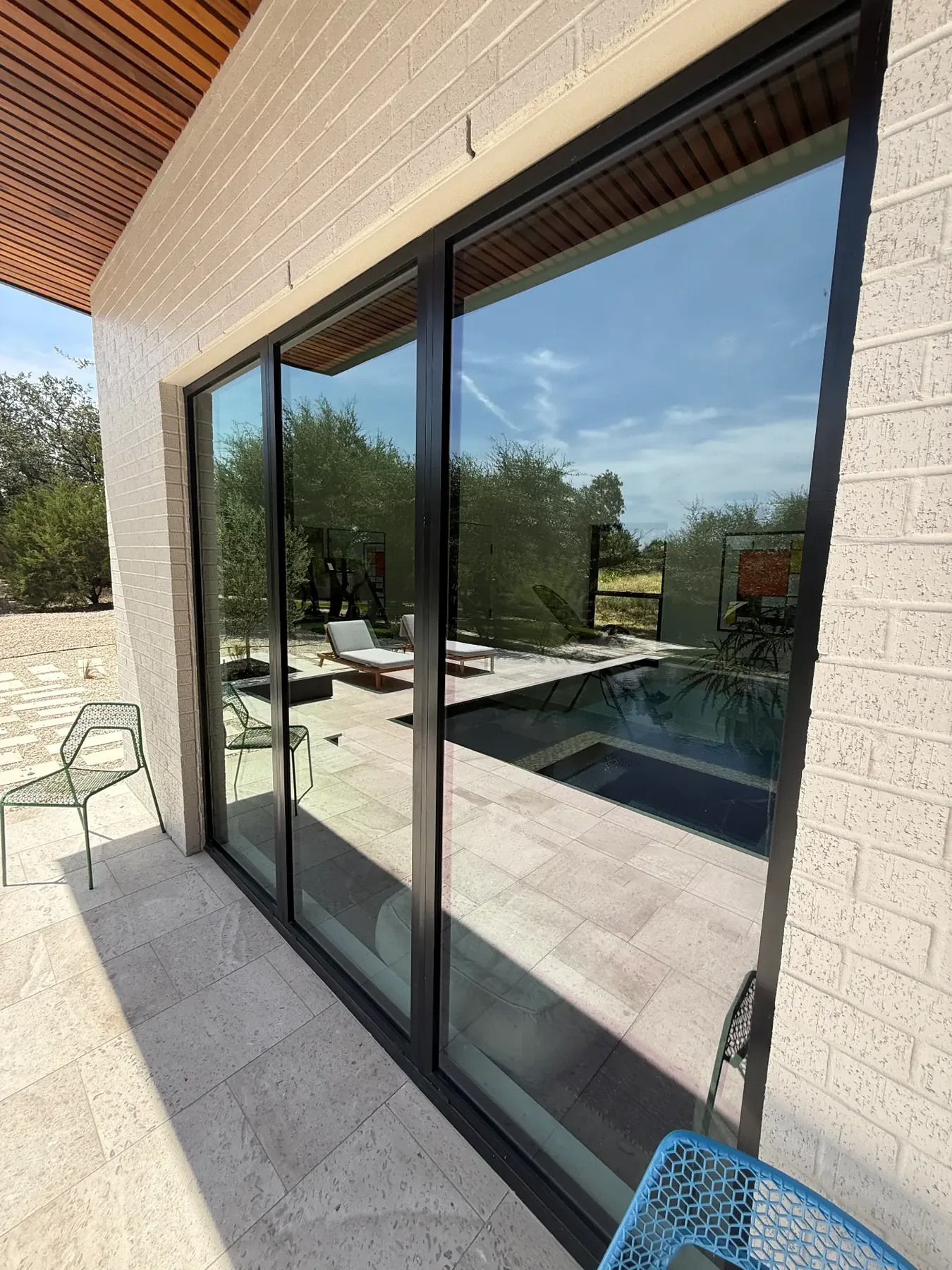 Full-height glass doors reflecting the pool and terrace of a South Austin outdoor living project